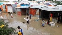 Anak-anak pengungsi menyeberangi air banjir di luar tempat penampungan sementara mereka di kamp Al Hidaya, pinggiran Mogadishu, Somalia, Senin (6/11/2023). (REUTERS/Feisal Omar)  