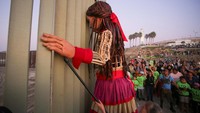 Orang-orang berkumpul di sekitar Little Amal di sepanjang tembok perbatasan antara Meksiko dan AS, di Tijuana, Meksiko, Senin (6/11/2023).  