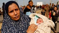Warga Palestina Um Hussein mengungsi sambil menggendong cucunya, Jumat (10/11/2023) waktu setempat. 