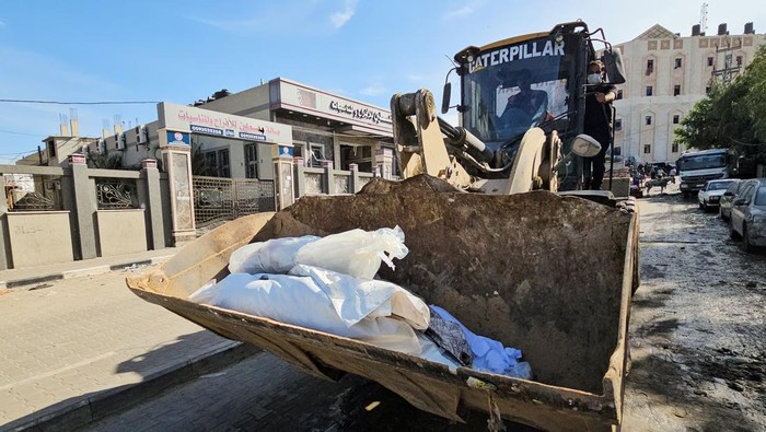 Korban Kebrutalan Israel Dikubur Massal, Jenazah Diangkut Ekskavator A machinery transports unidentified bodies of Palestinians killed in Israeli strikes before they are buried in a mass grave, in the northern Gaza Strip November 11, 2023. REUTERS/Anas al-Shareef