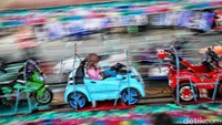 Seorang anak perempuan asik bermain di komidi putar berbentuk mobil-mobilan.  
