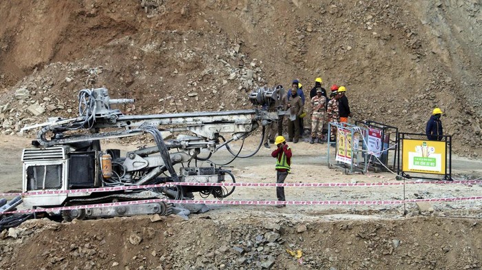 Hampir Seminggu, 40 Pekerja India Terjebak di Terowongan yang Ambruk Rescuers stand near heavy machinery at the site of an under-construction road tunnel that collapsed in mountainous Uttarakhand state, India, Friday, Nov. 17, 2023. Rescuers drilled deeper into the rubble of a collapsed road tunnel in northern India on Friday to fix wide pipes for 40 workers trapped underground for a sixth day to crawl to their freedom. (AP Photo)