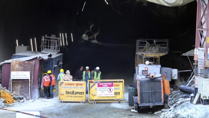 Hampir Seminggu, 40 Pekerja India Terjebak di Terowongan yang Ambruk Rescuers stand near heavy machinery at the site of an under-construction road tunnel that collapsed in mountainous Uttarakhand state, India, Friday, Nov. 17, 2023. Rescuers drilled deeper into the rubble of a collapsed road tunnel in northern India on Friday to fix wide pipes for 40 workers trapped underground for a sixth day to crawl to their freedom. (AP Photo)