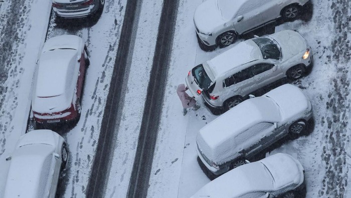 A woman cleans a car covered in snow during a first snowfall, amid Russia's attack on Ukraine, in Kyiv, Ukraine November 22, 2023. REUTERS/Gleb Garanich