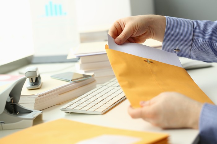 Businessperson opens yellow envelope with mail at workplace. Business correspondence and bank letter concept