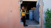 Seorang anak laki-laki Palestina melihat keluar dari lubang di dinding, sebuah sekolah yang rusak di Khan Younis, Gaza, 31 Oktober 2023. REUTERS/Ibraheem Abu Mustafa. 