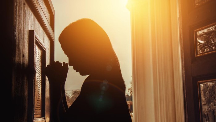 silhouette of woman kneeling and praying in modern church at sunset time