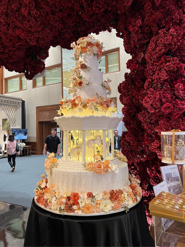 Unik, kue pernikahan yang satu ini memiliki desain carousel di bagian tengahnya. Dihiasi dengan lampu-lampu berwarna kuning dan juga bunga-bunga yang didominasi warna oranye, kue pernikahan tersebut tak kalah cantik dan menarik. Foto: Wolipop/Vina Oktiani