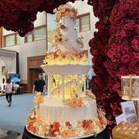 Unik, kue pernikahan yang satu ini memiliki desain carousel di bagian tengahnya. Dihiasi dengan lampu-lampu berwarna kuning dan juga bunga-bunga yang didominasi warna oranye, kue pernikahan tersebut tak kalah cantik dan menarik. Foto: Wolipop/Vina Oktiani