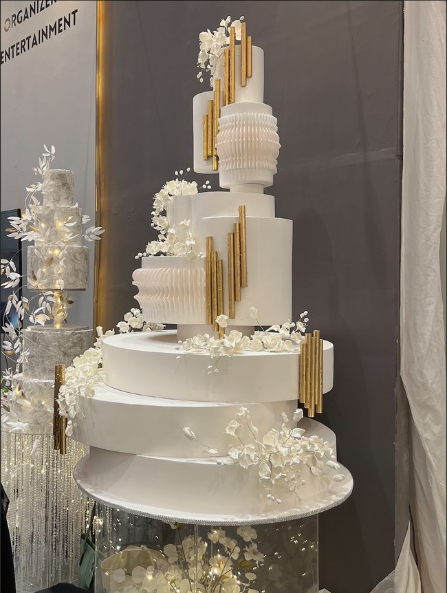 Simpel namun tetap elegan, kue pernikahan yang didominasi warna putih ini terlihat unik dengan susunan yang tidak simetris. Dengan tambahan sedikit ornamen berwarna gold membuat warna kue terlihat tidak monoton. Foto: Wolipop/Vina Oktiani