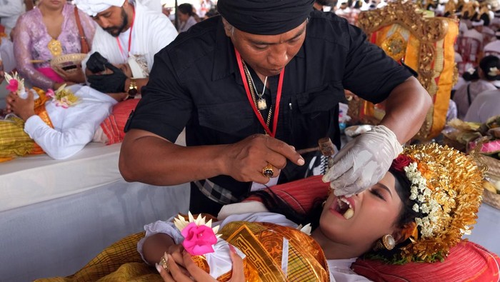 Seorang pemuda Bali melihat giginya melalui cermin saat ritual Metatah atau potong gigi massal yang bertepatan dengan hari suci Tumpek Wayang di Pura Agung Lokanatha, Bali, Sabtu (25/11/2023). Kegiatan yang digelar oleh Parisada Hindu Dharma Indonesia (PHDI) Kota Denpasar tersebut diikuti 204 umat Hindu sebagai upaya menghapus stigma bahwa ritual potong gigi di Bali menelan biaya besar dan cenderung dinilai menjadi beban bagi sebagian masyarakat yang belum paham maknanya. ANTARA FOTO/Nyoman Hendra Wibowo/aww.