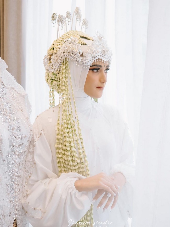 Nadya terlihat mengenakan hijab paris putih yang diikat rapi saat menjadi pengantin Sunda. Dalam foto ini, Nadya memakai wedding robe putih model dres dengan detail tangan berkerut. Ada detail lace dan pearl di bagian lengan. Foto: Dok. Instagram @nadyamustikarahayu.