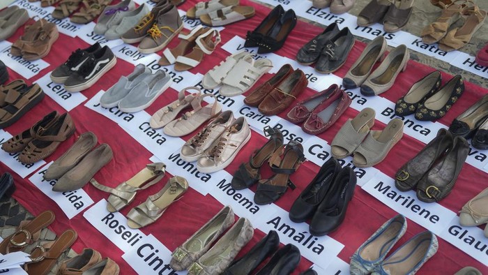 Instalasi Sepatu Peringati Hari Penghapusan Kekerasan Terhadap Perempuan Passersby look at an installation composed of the names of victims of gender violence and donated women's shoes, displayed on the edge of Copacabana beach to mark International Day for the Elimination of Violence against Women, in Rio de Janeiro, Brazil, Saturday, Nov. 25, 2023. (AP Photo/Silvia Izquierdo)