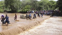 Orang-orang menyeberangi Sungai Muuoni yang banjir di daerah Mukaa, daerah Makueni, Kenya Timur, Jumat 24 November 2023. Jembatan yang putus akibat banjir memaksa warga melintasi sungai yang meluap.  