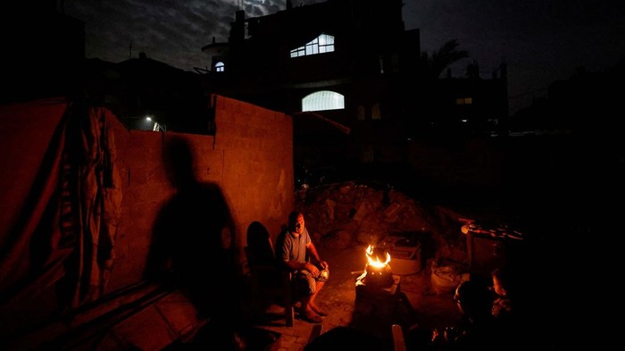 Palestinians sit next to a fire near the rubble of a house hit in an Israeli strike during the conflict, amid a temporary truce between Hamas and Israel, in Khan Younis in the southern Gaza Strip November 25, 2023. REUTERS/Mohammed Salem