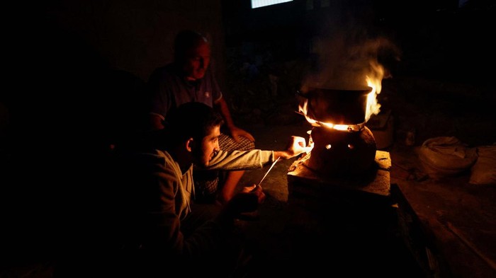 Warga Gaza Keluhkan Belum Masuknya Pasokan BBM Palestinians sit next to a fire near the rubble of a house hit in an Israeli strike during the conflict, amid a temporary truce between Hamas and Israel, in Khan Younis in the southern Gaza Strip November 25, 2023. REUTERS/Mohammed Salem