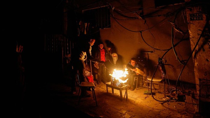 Palestinians sit next to a fire near the rubble of a house hit in an Israeli strike during the conflict, amid a temporary truce between Hamas and Israel, in Khan Younis in the southern Gaza Strip November 25, 2023. REUTERS/Mohammed Salem