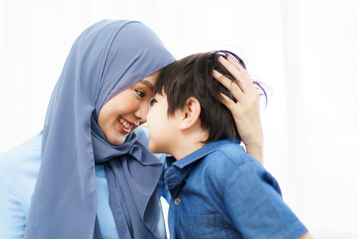 Happy cheerful Asian muslim family stay together in living room in weekend, Beautiful Asian woman muslim and lovely little boy portrait and looking at camera.