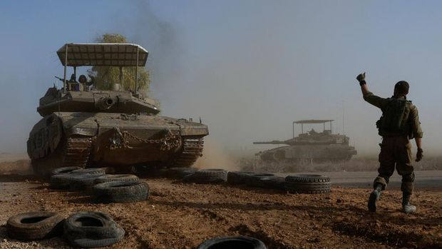 Seorang tentara Israel menunjuk ke arah awak tank saat melintasi jalan, sebagai bagian dari konvoi, di tengah konflik yang sedang berlangsung antara Israel dan kelompok Islam Palestina Hamas, dekat perbatasan Israel dengan Gaza selatan, di Israel, 4 Desember 2023. (REUTERS/Amir Cohen)