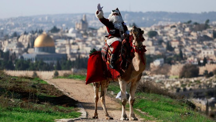 Issa Kassissieh, dressed as Santa Claus, sits astride a camel as he visits an olive grove overlooking the Dome of the Rock on Al-Aqsa compound, also known to Jews as the Temple Mount, in Jerusalem, December 4, 2023. REUTERS/Ammar Awad       TPX IMAGES OF THE DAY