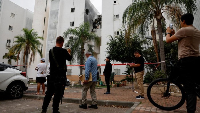 People stand next to a building which was hit by a rocket fired from Gaza today, amid the ongoing conflict between Israel and the Palestinian Islamist group Hamas, in Ashkelon, Israel, December 5, 2023. REUTERS/Amir Cohen      TPX IMAGES OF THE DAY