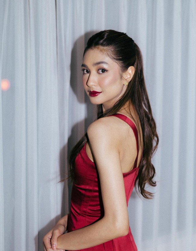 Untuk acara malam hari, Mikha Tambayong berganti busana dengan gaun merah marun berbahan satin. Gaun bergaya V-neck ini minim detail namun tetap terlihat elegan dari bahan satin. Foto: Instagram/@miktambayong @bagusboker