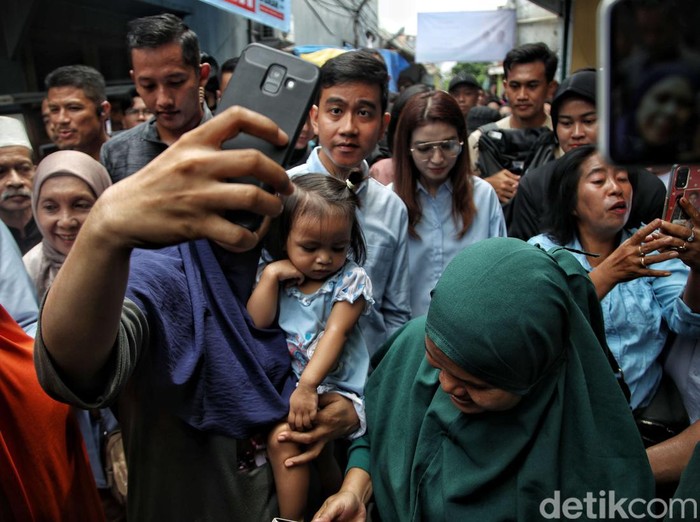 Calon wakil presiden nomor urut 2 Gibran Rakabuming Raka didampingi istri menyapa warga saat kampanye blusukan di kawasan Cempaka Putih Barat,  Jakarta Pusat, Sabtu (9/12/2023). Dalam kesempatan itu Gibran membagikan buku serta mensosialisasikan program kerja jika terpilih menjadi cawapres pada Pemilu 2024.