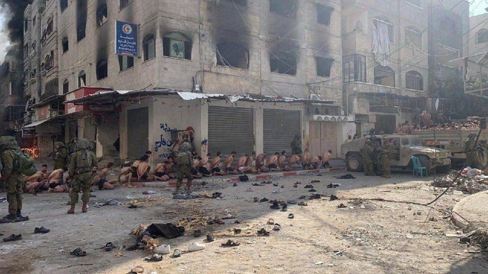 Captured and detained Palestinians sit on a street in Beit Lahia, northern Gaza Strip, as Israeli soldiers stand guard, amid the ongoing ground operation of the Israeli army against Palestinian Islamist group Hamas this handout image obtained by Reuters on December 8, 2023.   THIS IMAGE HAS BEEN SUPPLIED BY A THIRD PARTY. NO RESALES. NO ARCHIVES