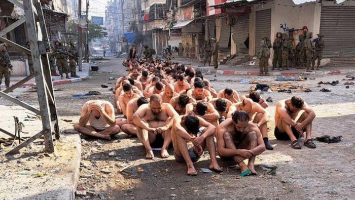 Captured and detained Palestinians sit on a street in Beit Lahia, northern Gaza Strip, as Israeli soldiers stand guard, amid the ongoing ground operation of the Israeli army against Palestinian Islamist group Hamas this handout image obtained by Reuters on December 8, 2023.   THIS IMAGE HAS BEEN SUPPLIED BY A THIRD PARTY. NO RESALES. NO ARCHIVES