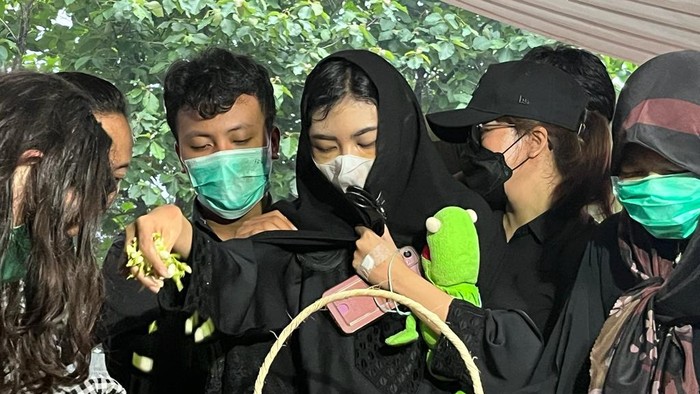Ibunda menarburkan bunga sambil memegang boneka hijau saat pemakaman 4 anak yang dibunuh suaminya (Rumondang/detikcom)