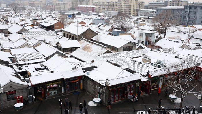 A staff member sweeps snow from a bench at a rooftop of a restaurant, on a snowy day in Beijing, China December 11, 2023. REUTERS/Tingshu Wang