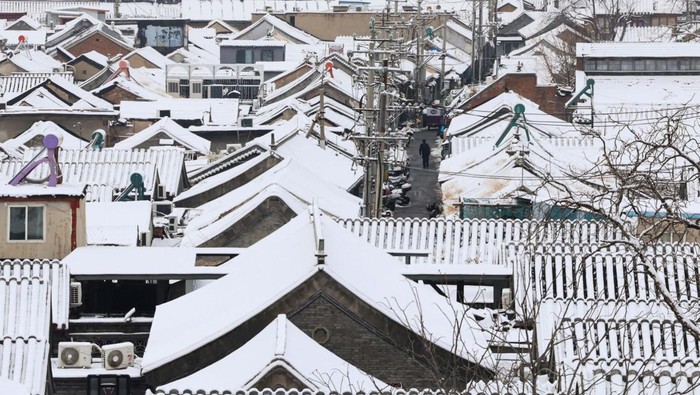 A staff member sweeps snow from a bench at a rooftop of a restaurant, on a snowy day in Beijing, China December 11, 2023. REUTERS/Tingshu Wang