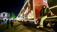 Orang-orang berpose untuk berfoto di samping kereta wisata La Sabana yang dihiasi lampu Natal di Bogota, Kolombia, Senin (11/12/2023).