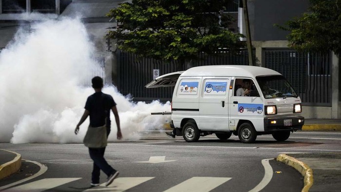 A motorcyclist drives past clouds of insecticide during a fumigation campaign against dengue-promoting mosquitoes, in the Altamira neighborhood of Caracas, Venezuela, Tuesday, Dec. 12, 2023. (AP Photo/Matias Delacroix)