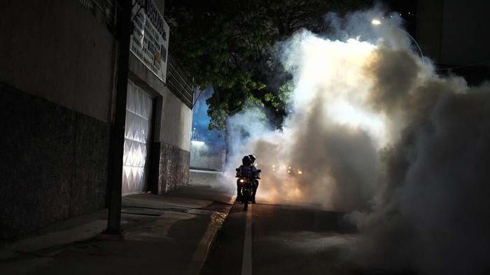 A motorcyclist drives past clouds of insecticide during a fumigation campaign against dengue-promoting mosquitoes, in the Altamira neighborhood of Caracas, Venezuela, Tuesday, Dec. 12, 2023. (AP Photo/Matias Delacroix)