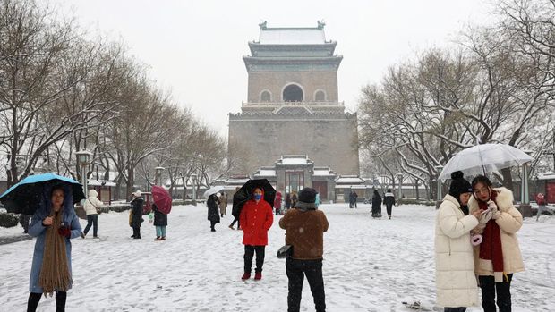 Orang-orang berjalan melewati Menara Lonceng di tengah hujan salju di Beijing, Cina 13 Desember 2023. (REUTERS/Tingshu Wang)