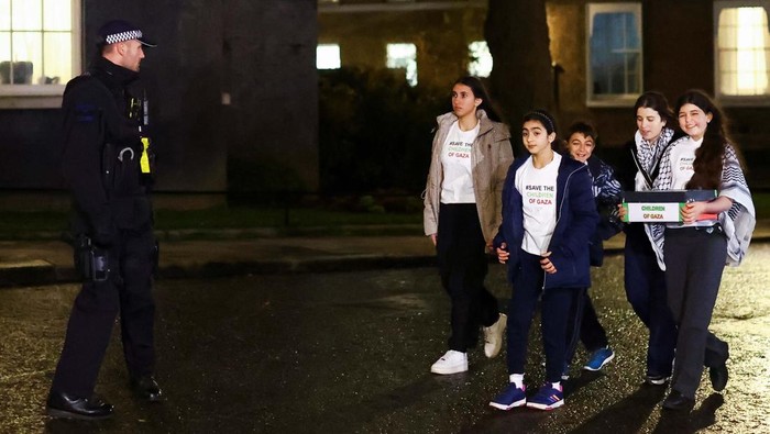 Children pose for a picture with a doorman as they arrive at Downing Street to hand in a petition asking the British Prime Minister Rishi Sunak for a ceasefire in Gaza, in London, Britain, December 13, 2023. REUTERS/Hannah McKay