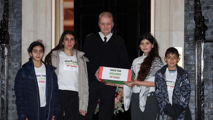 Serahkan Petisi, Anak-anak Minta Gencatan Senjata di Gaza Children pose for a picture with a doorman as they arrive at Downing Street to hand in a petition asking the British Prime Minister Rishi Sunak for a ceasefire in Gaza, in London, Britain, December 13, 2023. REUTERS/Hannah McKay