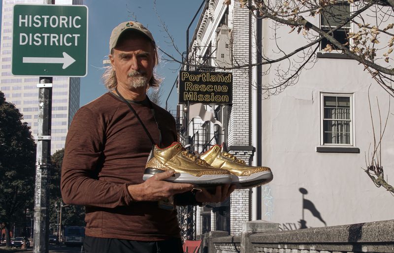 This photo provided by the Portland Rescue Mission shows James Free posing for a photo with a pair of of gold Nike Air Jordan 3 sneakers at the Portland Rescue Mission on Sunday, Oct. 30, 2023, in Portland, Ore.  A pair of rare Nike sneakers donated to a homeless shelter in Portland, Oregon, are up for auction and are expected to raise as much as $20,000. Why? They were custom-made for filmmaker Spike Lee. (Aaron Ankrom/Portland Rescue Mission via AP)