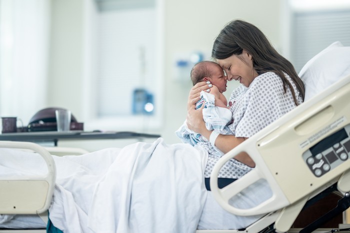 Newborn baby in delivery room.Blurred Mother background giving birth to a baby and kiss her baby. Woman pregnant patient in a hospital. Parent and infant first moments of bonding.
