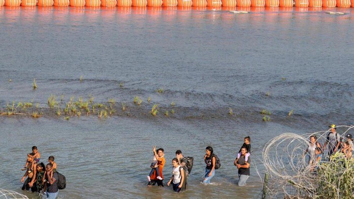 Migrants walk between concertina wire and a string of buoys placed on the water along the Rio Grande river with Mexico in Eagle Pass, Texas © SUZANNE CORDEIRO / AFP