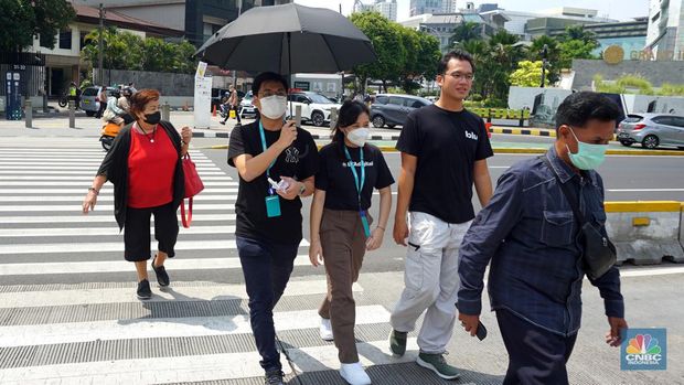 Pejalan kaki menggunakan payung untuk menghindari terik matahari di kawasan Jembatan Pinisi di halte busway Karet, Jakarta, Selasa (19/12/2023). (CNBC Indonesia/Muhammad Sabki)
