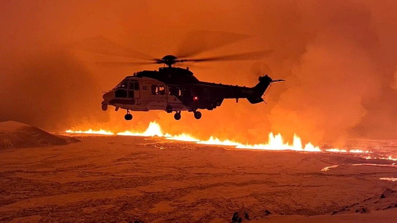 A helicopter flies near a volcano spewing lava and smoke as it erupts near Grindavik, Iceland, December 19, 2023. (Icelandic Coast Guard/Handout via REUTERS THIS IMAGE HAS BEEN SUPPLIED BY A THIRD PARTY. NO RESALES. NO ARCHIVES. MANDATORY CREDIT