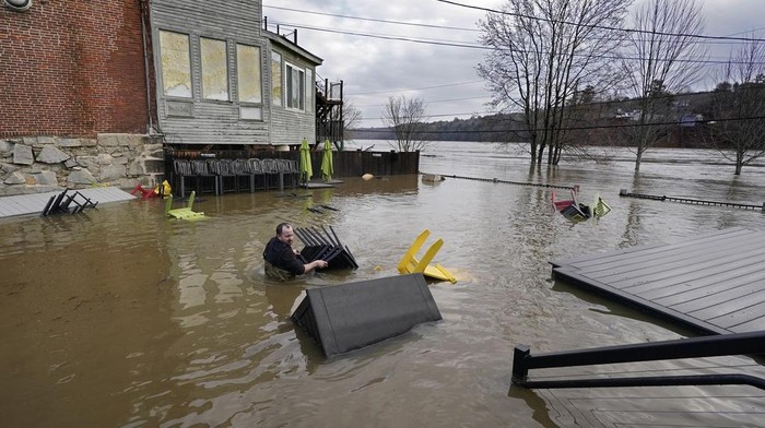 Penampakan Banjir Landa Wilayah Timur Laut AS Nathan Sennett wades to retrieve furniture in hip-deep water on the patio of the Quarry Tap Room, Tuesday, Dec. 19, 2023, in Hallowell, Maine. Waters continue to rise in the Kennebec River following Monday's severe storm. (AP Photo/Robert F. Bukaty)