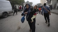 Seorang ibu dan anaknya lari ketakutan dari gempuran Israel di perbatasan Rafah, Gaza. (AP Photo/Fatima Shbair)