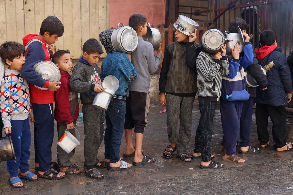 Anak-anak Palestina memegang panci saat mereka mengantri untuk menerima makanan yang dimasak oleh dapur amal, di tengah kekurangan pasokan makanan, saat konflik antara Israel dan Hamas berlanjut, di Rafah di selatan Jalur Gaza 14 Desember 2023. (REUTERS/Saleh Salem)