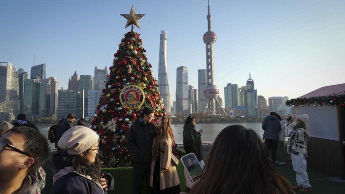 Melihat Perayaan Natal di China People take pictures of a Christmas tree decorated along the Shanghai Bund against the Pudong Financial District in Shanghai on Dec. 17, 2023. Like other western festivals, Christmas is not traditionally celebrated in China, but it has been a common thing among young Chinese in big cities like Shanghai. (AP Photo/Wayne Zhang)