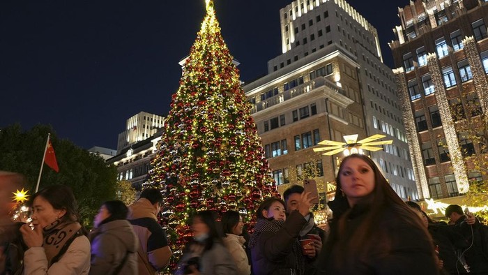 Melihat Perayaan Natal di China People take pictures of a Christmas tree decorated along the Shanghai Bund against the Pudong Financial District in Shanghai on Dec. 17, 2023. Like other western festivals, Christmas is not traditionally celebrated in China, but it has been a common thing among young Chinese in big cities like Shanghai. (AP Photo/Wayne Zhang)
