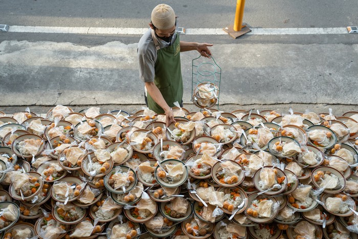 a man preparing takjil food at the jogokariyan mosque, so many stacks of plates filled. : Yogyakarta - Indonesia, April 04, 2023