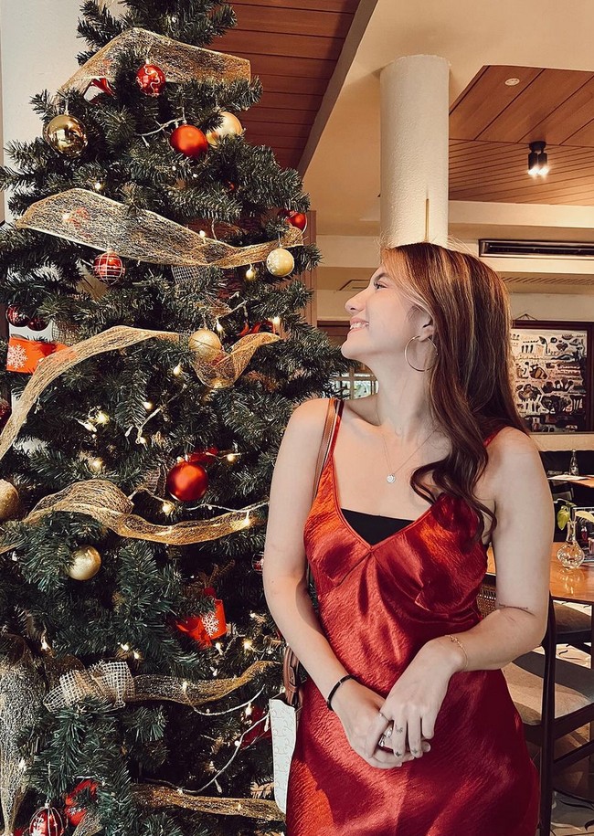 Cassandra Lee tampil dengan shift dress merah dipadu dalaman warna hitam. Sebagai pelengkap penampilan, aktris 22 tahun ini memakai anting loop dan kalung. Cassandra tampak berpose di samping pohon Natal. Foto: Instagram